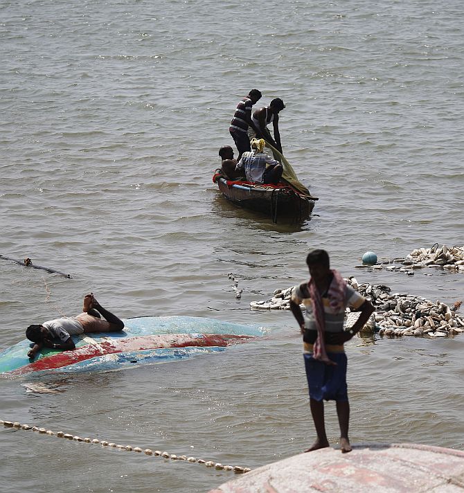 A fisherman lies on his overturned boat as others take out their fishing nets from the sea after Cyclone Phailin hit Gopalpur port in Ganjam district