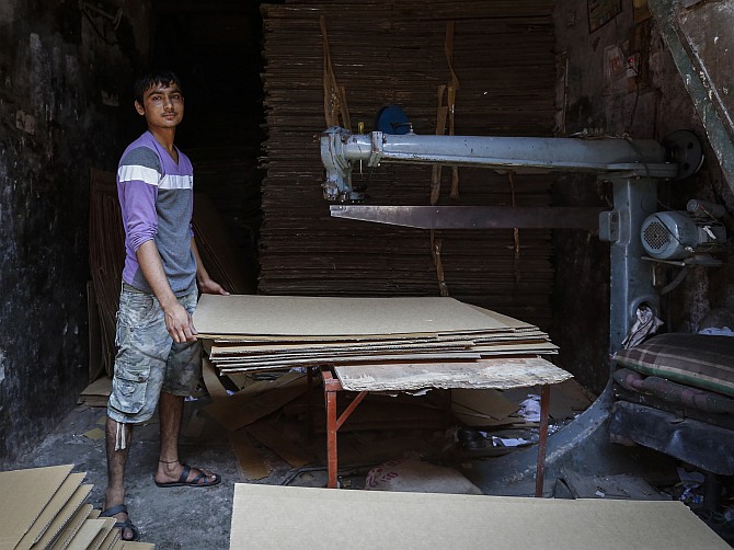 Riyazuddin, an 18-year-old worker, poses next to a cardboard box manufacturing unit at a slum in Mumbai.