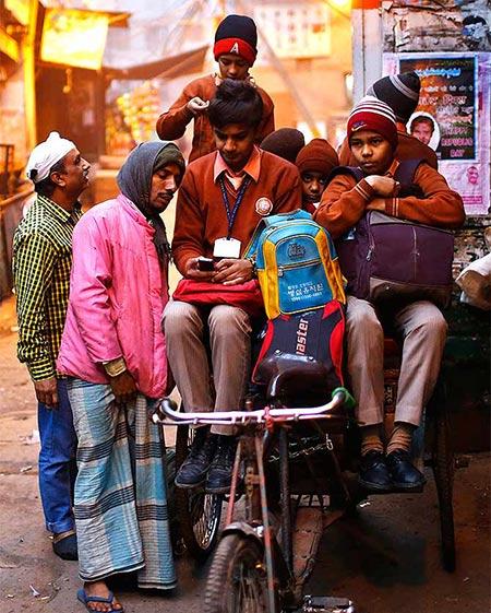 A school boy shows his mobile phone to a rickshaw puller who takes him and other students to school on a cold winter morning in old Delhi.