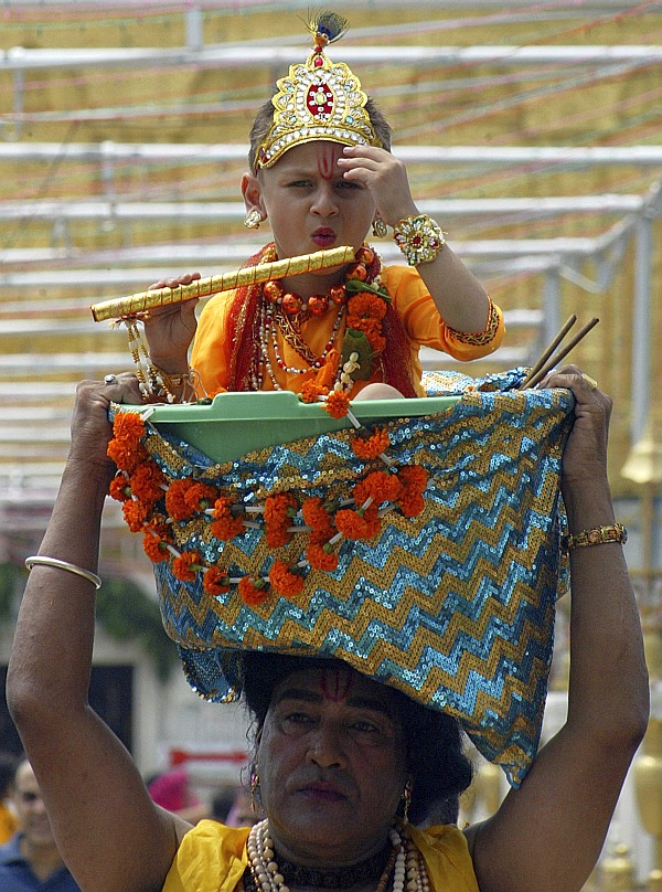 A devotee carries a child dressed as Hindu god Krishna in a basket at the Durgiana temple during the celebrations of Janmashtami in Amritsar 