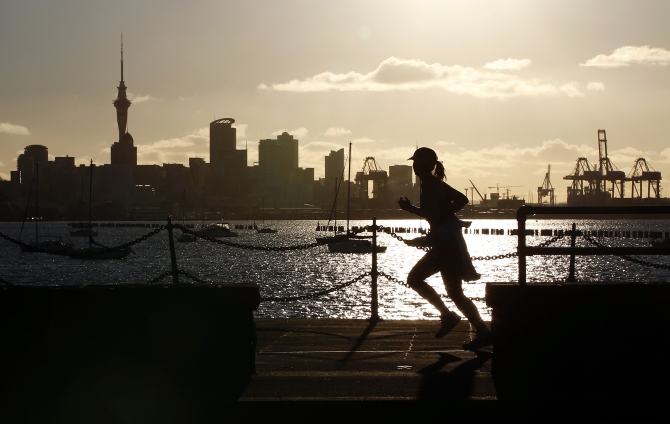 A jogger runs along the seawall in Auckland, with the city skyline in the background.