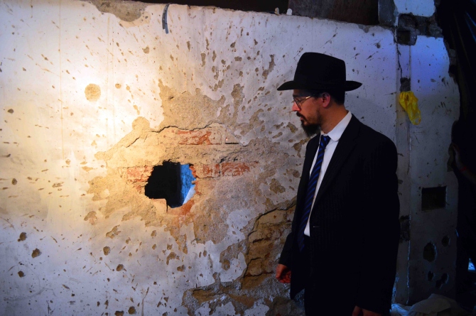 A rabbi touches a wall riddled with bullet holes in front of Nariman House