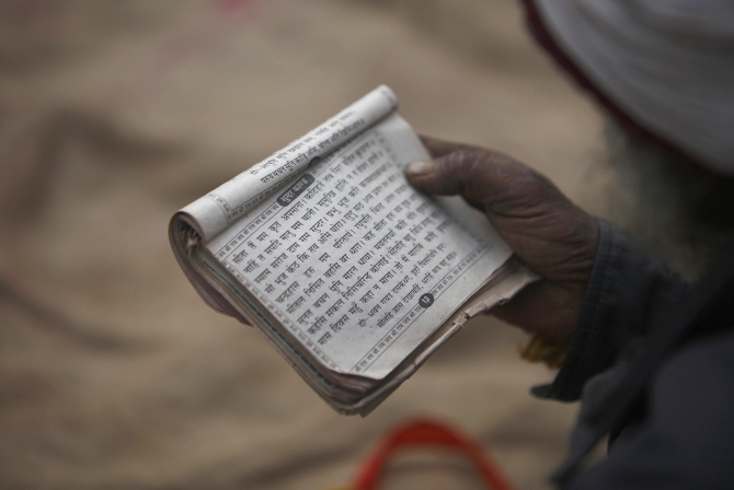 A holy man recites prayers from a holy book at the premises of a temple.