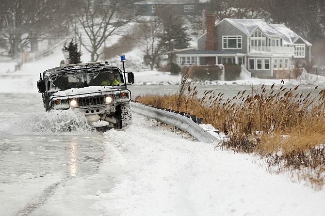 A police vehicle drives through a flooded street during a winter nor'easter snow storm in Scituate, Massachusetts 