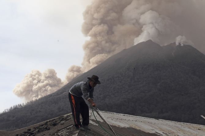 A villager clears ash on the roof of his house with water during the eruption of Mount Sinabung at Kuta Rakyat village in Karo district, Indonesia's North Sumatra province.