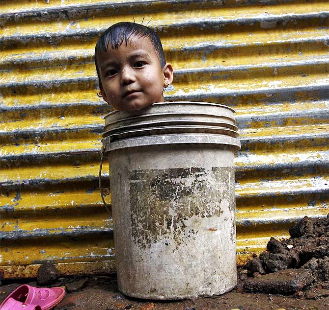 A boy waits for his mother to fetch water from a nearby hand pump to bathe him, outside a makeshift hut in Chennai.