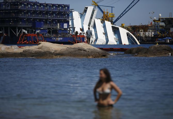 A woman stands on the beach as the capsized cruise liner Costa Concordia lies surrounded by cranes outside Giglio harbour. 