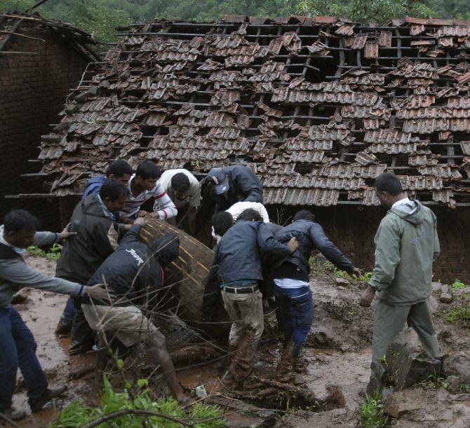Rescue workers and volunteers clear the debris from the site of a landslide at Malin village
