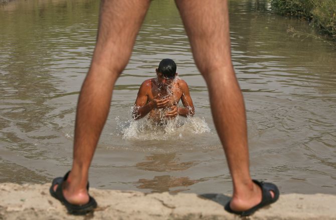 A man bathes in a water canal on a hot summer day on the outskirts of Jammu