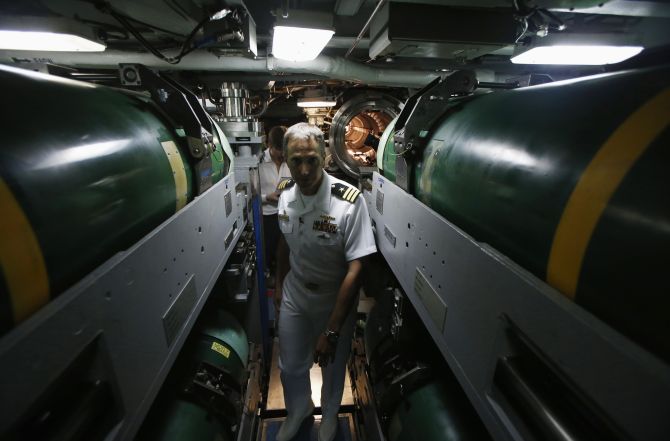 Commanding Officer Richard Rhinehart walks between rows of torpedoes in the torpedo room onboard the USS North Carolina (SSN-777) submarine docked at Changi Naval Base in Singapore