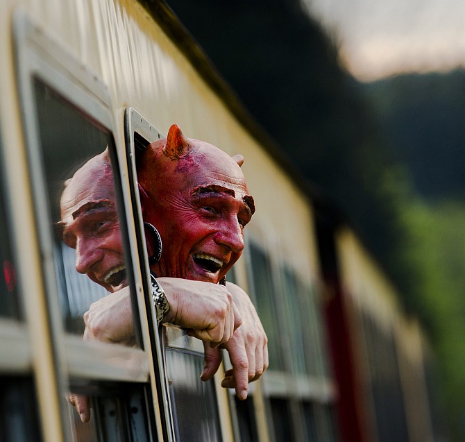 Man with a devil make-up looks out of a HSB light railway carriage as he travels through the Harz mountains to celebrate the Walpurgisnacht pagan festival