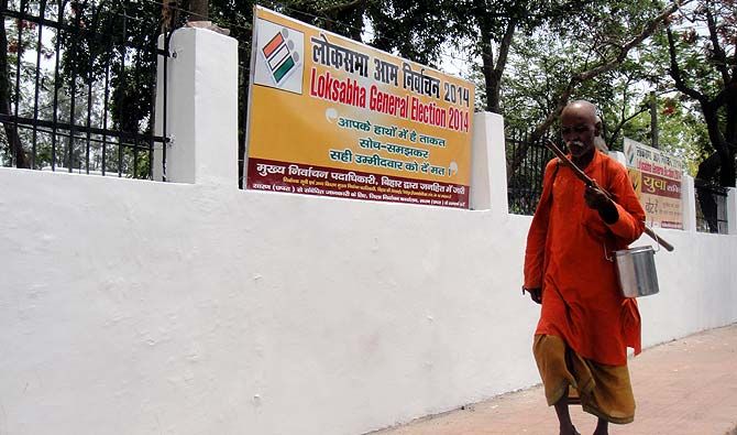 A man in saffron robes walks past a poll banner at the Saran Collectorate. Photograph: Archana Masih/Rediff.com