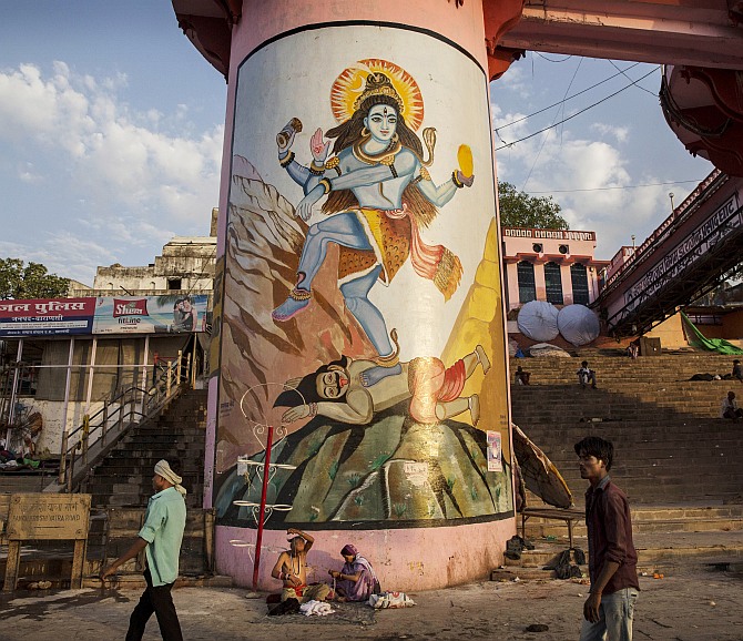 People walk passed a large mural of the Lord Shiva along the Ganga River in Varanasi