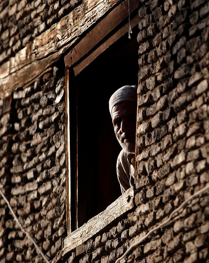A Kashmiri man looks out of the window of his house