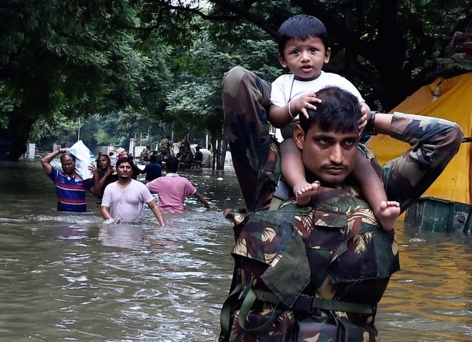 Army personnel carry children on their shoulders as they wade through flood waters in rain-hit Chennai on Thursday. 