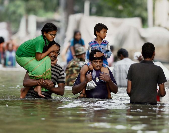 Residents carry their children on their shoulders as they wade through a flooded street in Chennai. Photograph: PTI