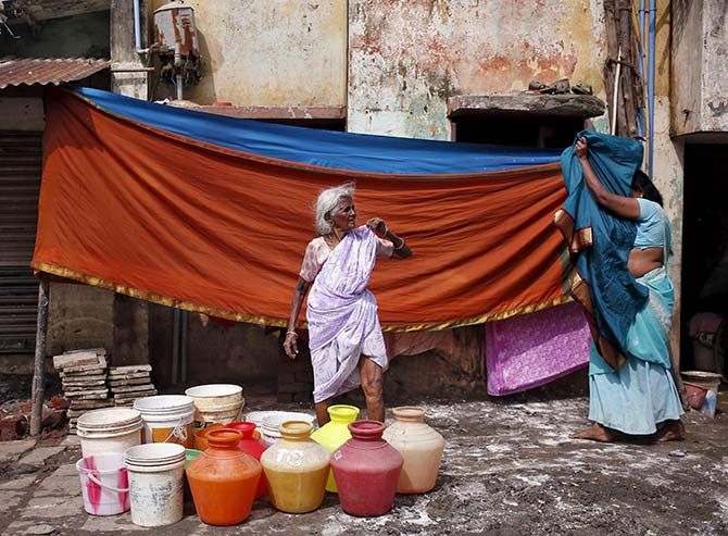 A woman waits outside her house for a water tanker to fill her containers with drinking water.
