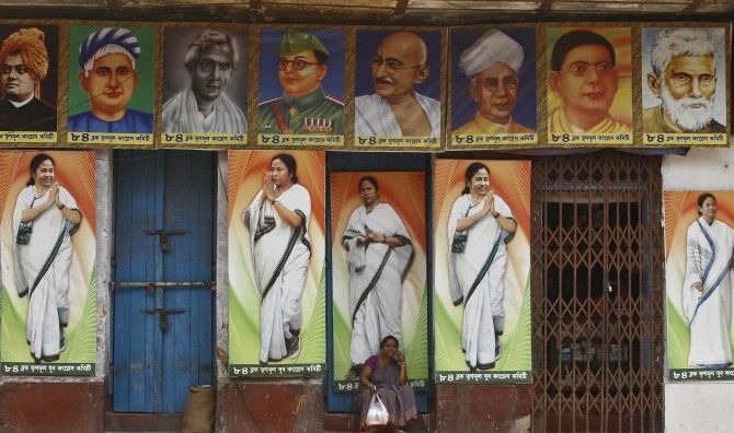 A woman sits under a building decorated with pictures of Mamata Banerjee.