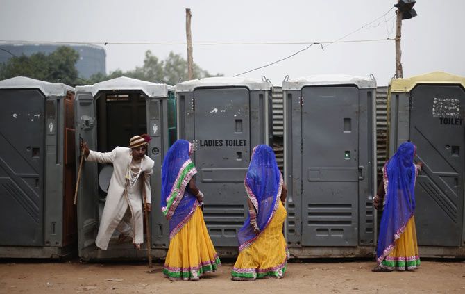 A groom emerges from a toilet, as brides stand outside the venue of a mass wedding ceremony, Ramlila grounds, New Delhi, June 15, 2014. Photo: Adnan Abidi/Reuters