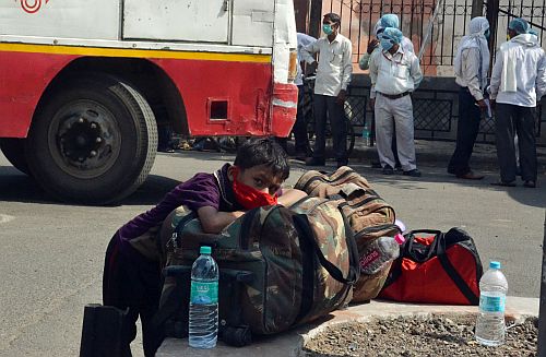 A boy rests on his bags as he waits to board a bus.