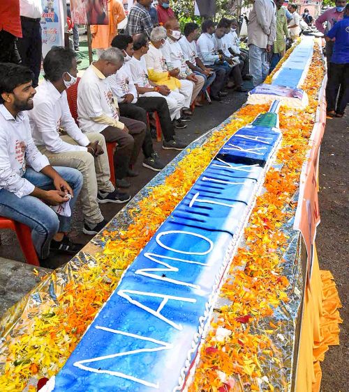 BJP workers sit beside a vaccine shaped cake on eve of PM's b'day