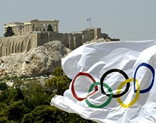 An Olympic flag blows in the wind in front of the hill of the Acropolis.