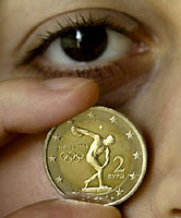 A woman displays a two Euro commemorative coin launched to celebrate the return of the Olympic Games to their birthplace in Athens