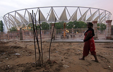 A woman walks past the Jawaharlal Nehru Stadium that is still under construction