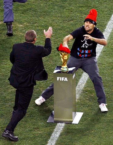 A pitch intruder covers the World Cup trophy with a cap