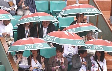 Spectators shelter themselves from the rain with umbrellas during the French Open tennis tournament at Roland Garros in Paris