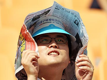 A spectator uses a newspaper to take shelter from the sun as he watches the action at the Daegu Stadium on Monday