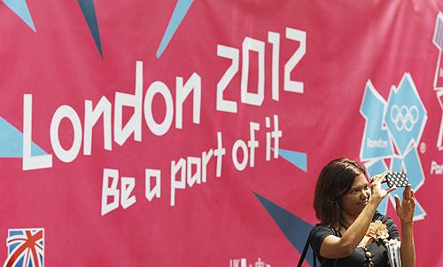 A woman takes a photo in front of a banner showcasing the London 2012 Olympics