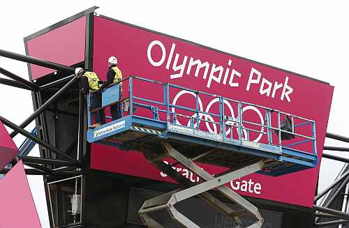 Worker adjusts his position on cherry picker in front of one of the signs at the entrance to the Olympic Park
