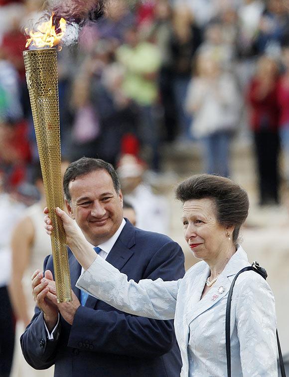 Britain's Princess Anne raises a torch with the Olympic Flame next to Spyros Kapralos, head of the Greek Olympic Committee, during an Olympic flame handover ceremony at the Panathenaic stadium on Thursday