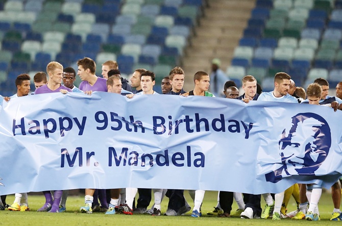 Players carry a birthday banner for Mandela during the Nelson Mandela Football Invitational match