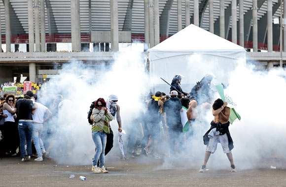 Activists and students stand in a cloud of tear gas as they clash with riot police outside the Mane Garrincha National Stadium in Brasilia