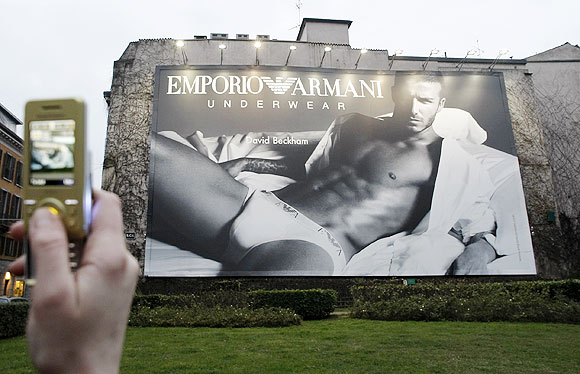 A girl takes a picture with a mobile phone of a maxi advertising campaign for Armani underwear with British soccer player David Beckham in downtown Milan, January 15, 2008