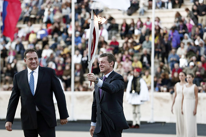 Russia's Deputy Prime Minister Dmitry Kozak (centre) raises an Olympic torch for the Sochi 2014 Winter Games next to President of the Greek Olympic Committee Spyros Kapralos during a handover ceremony at the Panathenean stadium in Athens on Saturday