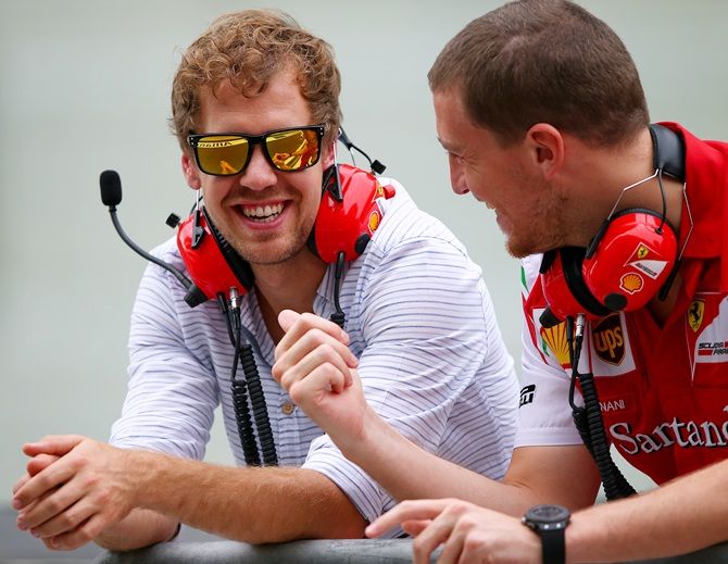 Sebastian Vettel of Germany smiles as he speaks with members of Ferrari team