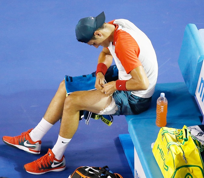 Bernard Tomic of Australia removes strapping from his leg