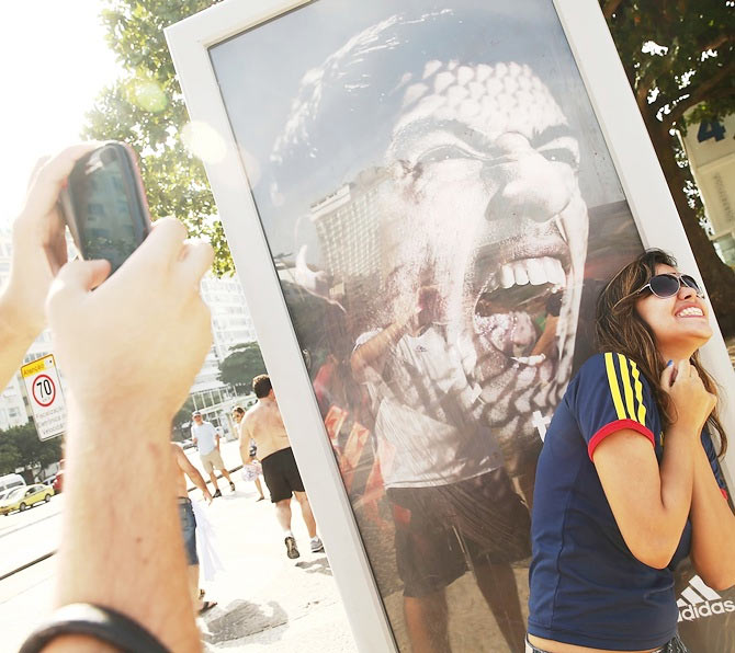 A woman takes a photo next to an advertisement featuring Uruguay's Luis Suarez, mocking the biting incident against opponent Giorgio Chiellini