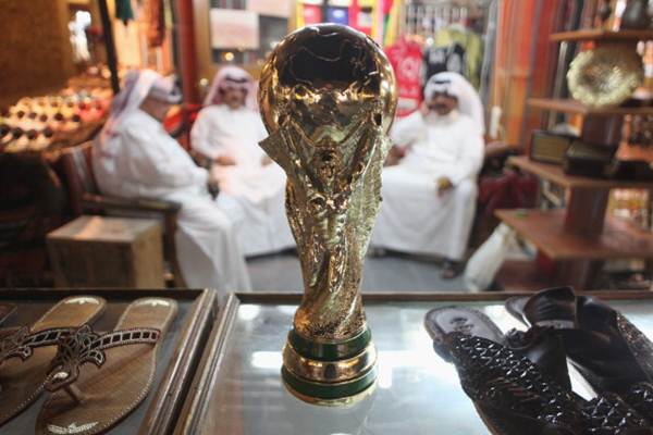 Arab men sit at a shoemaker's stall with a replica of the FIFA World Cup trophy in the Souq Waqif traditional market