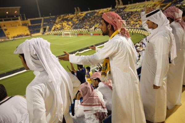Fans wearing traditional local dress react to play during a match at Al Gharafa Stadium