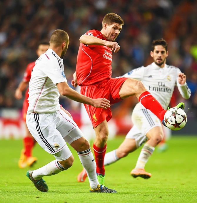 Steven Gerrard of Liverpool kicks the ball under pressure from Karim Benzema of Real Madrid