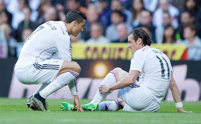 Gareth Bale (real) of Real Madrid touches his leg as his teammate Cristiano Ronaldo (left) assists him during their La Liga match at Estadio Santiago Bernabeu on Saturday
