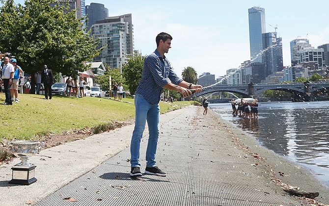 Novak Djokovic of Serbia sprays champagne after posing with the Norman Brookes Challenge Cup at the Melbourne University Boat Club, on Monday