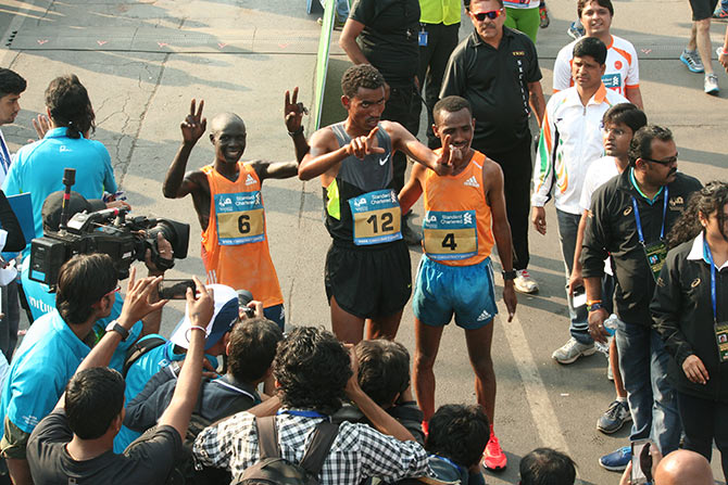 Ethiopia's Tesfaye Abera, compatriot  Dereje Debele and Kenyan Luke Kibet celebrate at the finish  line after completing the Mumbai Marathon on Sunday