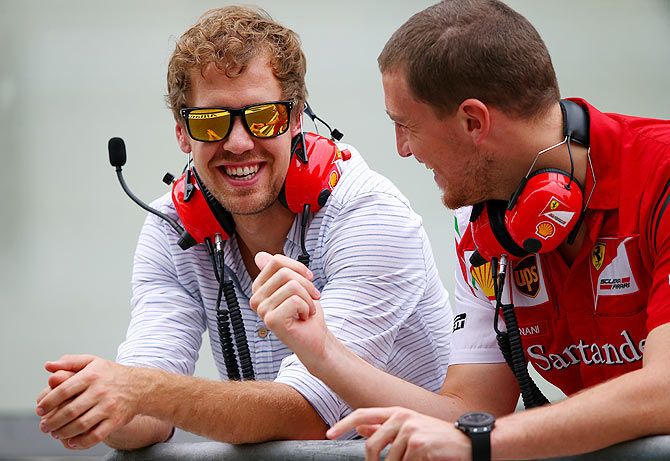 Sebastian Vettel of Germany and Infiniti Red Bull Racing smiles as he speaks with members of the Ferrari team