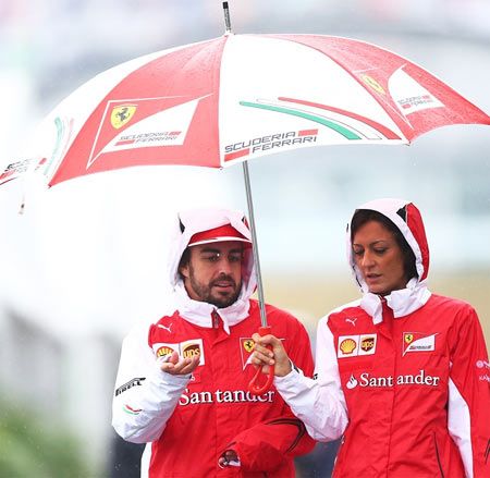 Fernando Alonso of Spain and Ferrari walks across a wet paddock