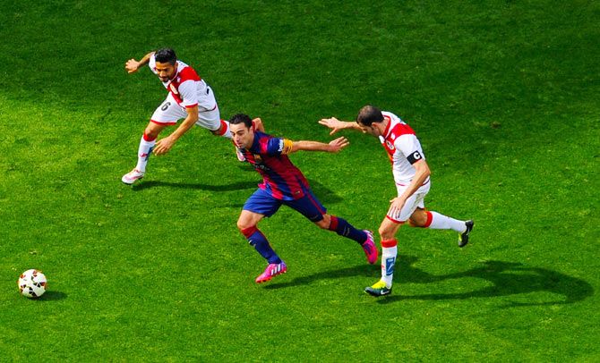 FC Barcelona's Xavi Hernandez competes for the ball with Rayo Vallecano's Javier Ignacio Aquino (left) and Roberto Trashorras
